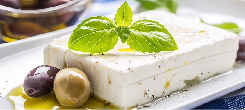 Feta cheese on a plate with olive oil and olives, garnished with basil.